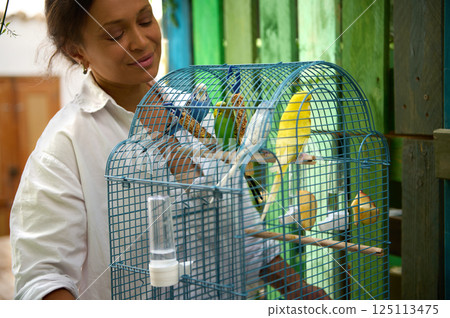 Woman Caring for Colorful Birds in a Cage Outdoors 125113475