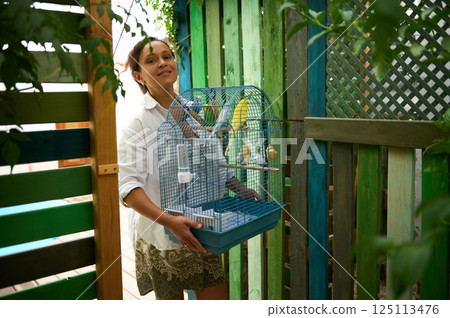 Woman Holding a Birdcage Outdoors in a Wooden Fenced Area 125113476