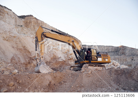 Middle aged man is with excavator in the quarry at daytime Middle aged man is with excavator in the quarry at daytime 125113606