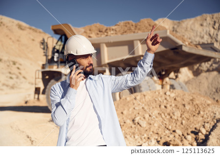 Engineer is with the phone. Man in uniform is working in the quarry at daytime Engineer is with the phone. Man in uniform is working in the quarry at daytime 125113625
