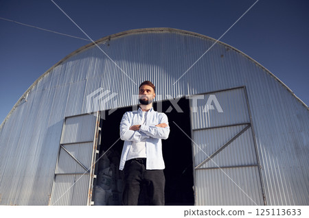 Man in formal clothes is standing against hangar at daytime 125113633