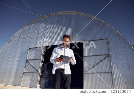 Man in formal clothes is standing against hangar at daytime 125113634