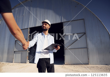 Two people standing against hangar and making a deal by handshale Two people standing against hangar and making a deal by handshale 125113635