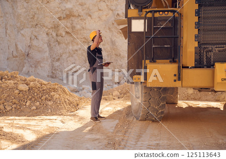 With documents near the haul truck. Man in uniform is working in the quarry at daytime 125113643