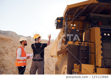 Looking at big haul truck. Two men in uniform are working together in the quarry 125113660