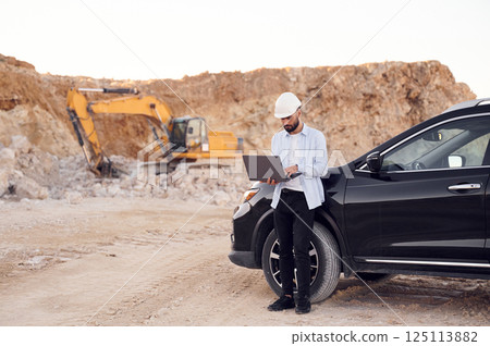 Using laptop. Man in uniform is working in the quarry at daytime 125113882