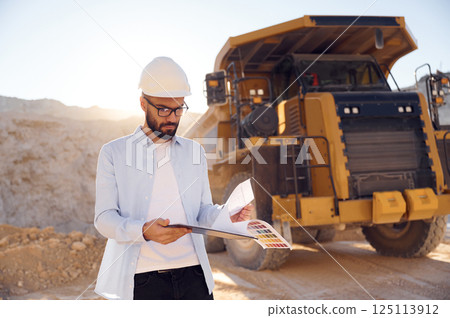 Smart man in glasses and in uniform is working in the quarry at daytime Smart man in glasses and in uniform is working in the quarry at daytime 125113912