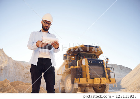 Smart person is with documents in hands. Man in uniform is working in the quarry at daytime 125113925