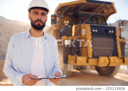 Smart person is with documents in hands. Man in uniform is working in the quarry at daytime 125113926