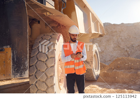 Using smartphone. Man in uniform is working in the quarry at daytime Using smartphone. Man in uniform is working in the quarry at daytime 125113942