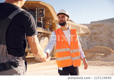 Making a deal. Doing handshake. Two men in uniform are working together in the quarry Making a deal. Doing handshake. Two men in uniform are working together in the quarry 125114049