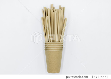 Paper cups and paper straws on white background, Accessories for drinking outdoors, Ecology recycling eco friendly, Eco friendly reusable paper straws, Kraft paper straw for drinking coffee or tea. 125114332