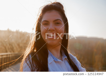 Joyful young woman smiling outdoors at sunset Joyful young woman smiling outdoors at sunset 125114947