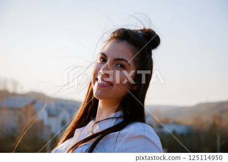 Woman smiling outdoors in sunset light with mountain view background Woman smiling outdoors in sunset light with mountain view background 125114950