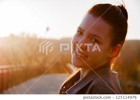 Smiling woman enjoying sunset outdoors with warm golden light 125114976