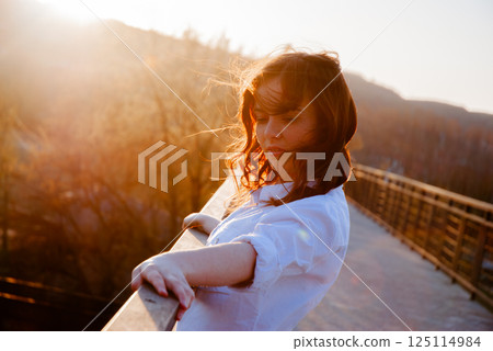 Tranquil woman on bridge at sunset during a peaceful evening Tranquil woman on bridge at sunset during a peaceful evening 125114984