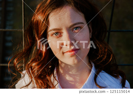 Thoughtful woman with wavy red hair in sunlit portrait 125115014