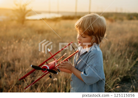 Smiling preschool child boy plays with craft wooden retro styled airplane 125115056