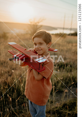 Smiling preschool child boy plays with craft wooden retro styled airplane 125115066