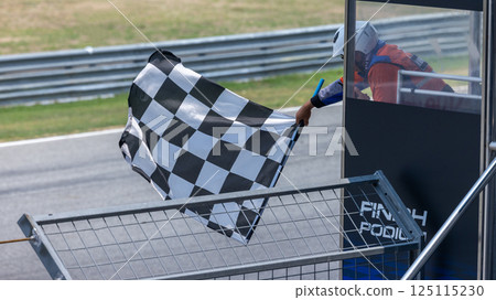 Man holding and waving checkered race flag on finish podium, Finish line and checkered flag, Race flag at the finish line on a race track, Victory achievement success motorsport. 125115230