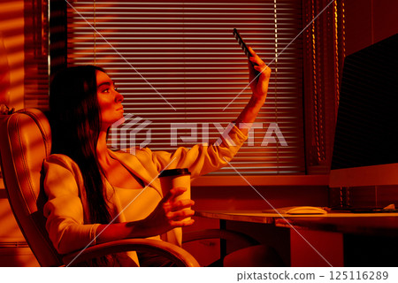 Confident Woman Taking Selfie in Office Chair with Coffee. Confident Woman Taking Selfie in Office Chair with Coffee. 125116289