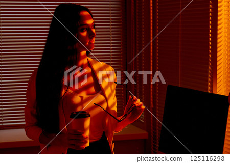 Confident Business Woman Holding Glasses and Coffee in Sunset Office. Confident Business Woman Holding Glasses and Coffee in Sunset Office. 125116298
