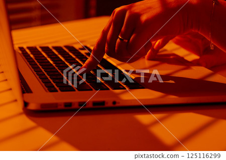 Female Hand Typing on Laptop in Sunset Light with Shadow Patterns. 125116299
