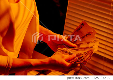 Female Hands Holding Euro and Dollar Banknotes in Warm Office Light. 125116309