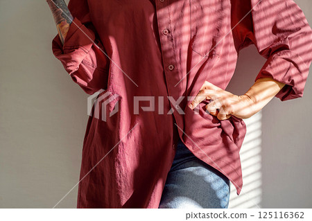 Cropped Woman in Maroon Shirt Poses with Hand on Hip, Artistic Lighting Accentuates Her Style. 125116362