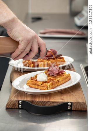 Chef pouring sauce on waffle with brisket 125117392