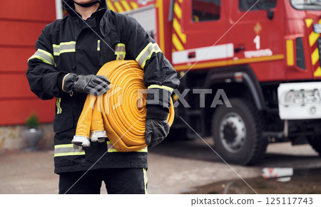 Outside near truck and with fire hose in hands. Woman in uniform is at work in department 125117743