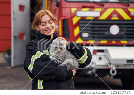 Coneption of animal care. Beautiful scottish fold cat in hands. Woman firefighter in uniform is at work in department Coneption of animal care. Beautiful scottish fold cat in hands. Woman firefighter in uniform is at work in department 125117755