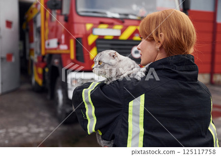 View from behind. Holding cat on shoulders. Woman firefighter in uniform is at work in department 125117758