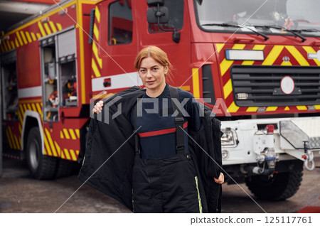 Taking off the protective clothes. Woman firefighter in uniform is at work in department 125117761