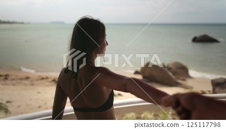 Woman in bikini stand on hotel villa balcony hold boyfriend hand show beautiful sea view sand beach ocean landscape. Travel Thailand exotic island. Couple tourist on summer vacation. Lifestyle holiday 125117798