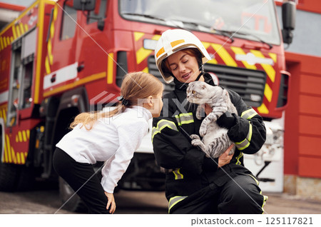 Near the truck. With scottish fold cat. Firefighter woman in uniform is with a little girl 125117821