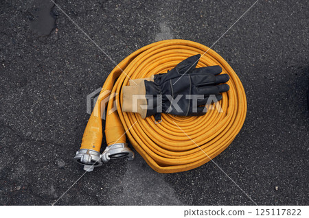 Top view of yellow fire hose with black gloves on it on the ground 125117822