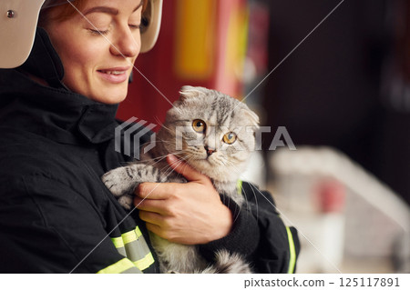 Holding beautiful scottish fold cat. Woman firefighter in uniform is at work in department Holding beautiful scottish fold cat. Woman firefighter in uniform is at work in department 125117891