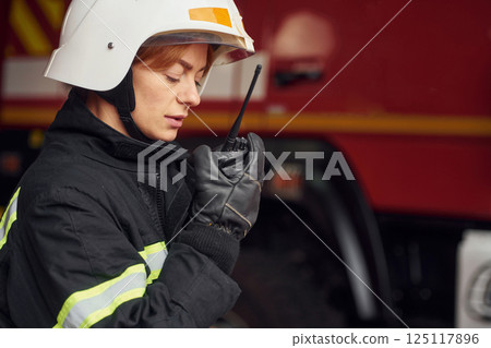 Using radio transmitter. Woman firefighter in uniform is at work in department 125117896