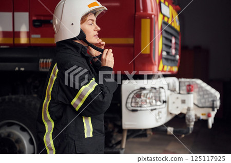 Wearing protective equipment. Woman firefighter in uniform is at work in department 125117925