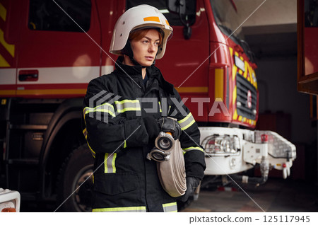 Grey colored fire hose is in the hands. Woman in uniform is at work in department 125117945