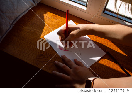 Preteen daughter carefully crafting mother's day, 8 march or birthday card for mom sitting by window at home. Concept of family love, tradition and celebration. Preteen daughter carefully crafting mother's day, 8 march or birthday card for mom sitting by window at home. Concept of family love, tradition and celebration. 125117949
