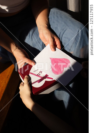 Young woman receiving gift box and handmade greeting card with painting from daughter for mother's day, 8 march, birthday. Close up. Young woman receiving gift box and handmade greeting card with painting from daughter for mother's day, 8 march, birthday. Close up. 125117955