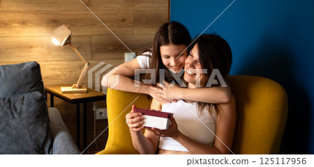 Happy mother's day. Preteen daughter hugs and congratulates moms giving her gift box. Motherhood concept. 125117956