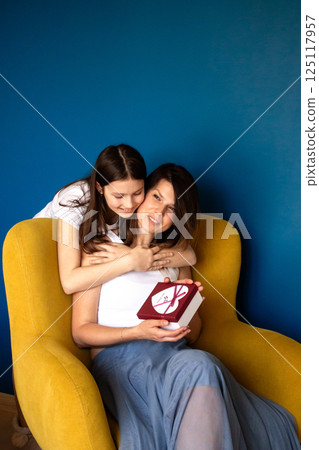 Happy mother's day. Preteen daughter hugs and congratulates moms giving her gift box. Motherhood concept. 125117957