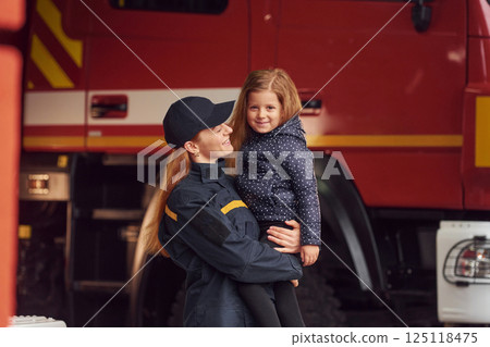 Firefighter woman in uniform is holding a little girl in the hands 125118475