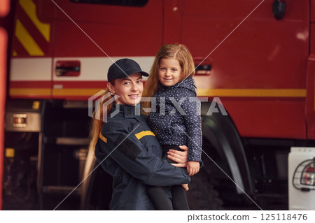Firefighter woman in uniform is holding a little girl in the hands 125118476