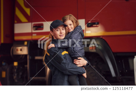 Firefighter woman in uniform is holding a little girl in the hands Firefighter woman in uniform is holding a little girl in the hands 125118477