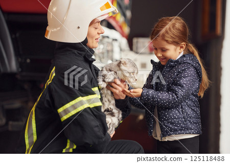 Rescued scottish fold cat. Firefighter woman in uniform is with a little girl 125118488