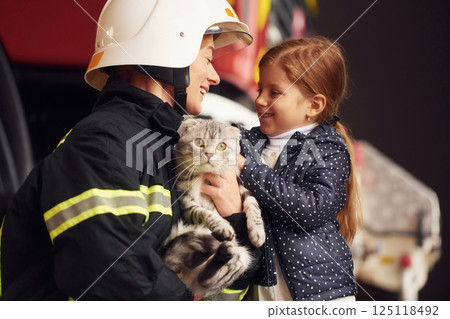 Giving beautiful scottish fold cat. Firefighter woman in uniform is with a little girl 125118492